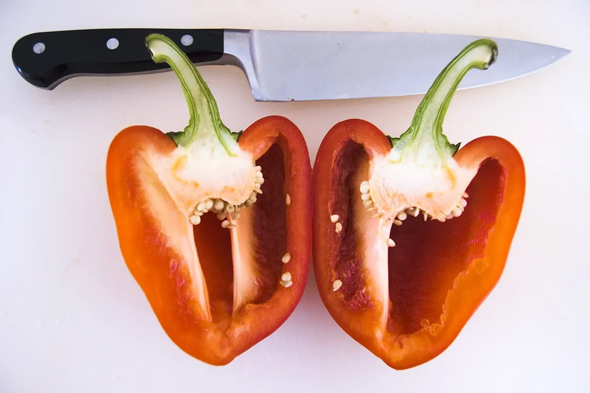 Poivron rouge cru coupé en deux à côté d’un couteau de cuisine